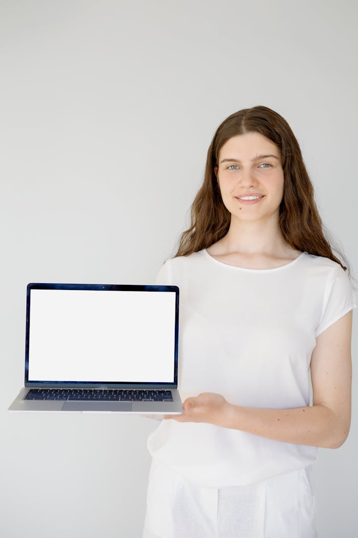 Portrait of a smiling woman holding a laptop with a blank screen, perfect for display mockups.